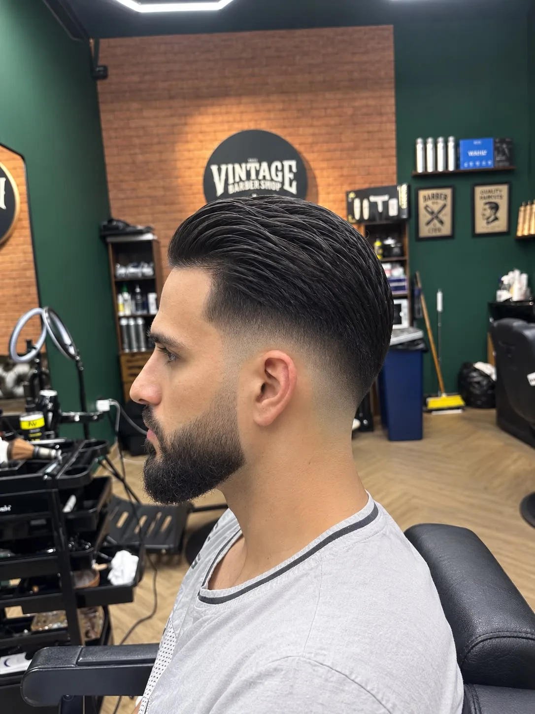 Side profile of longer hair swept back with a glossy finish, a fade behind the ear and a full beard